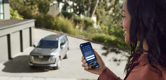 Woman is sitting inside the home looking out the window with a phone in her hand. On the phone is the OnStar Insurance website.