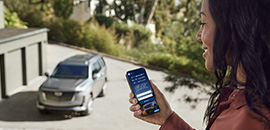 Woman is sitting inside the home looking out the window with a phone in her hand. On the phone is the OnStar Insurance website.